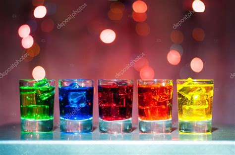 Five shots glasses full of assorted beverages and ice on golden blurred ...