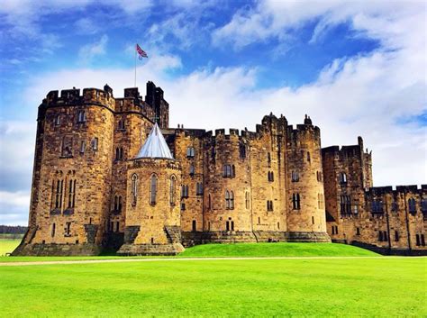 an old castle sitting on top of a lush green field under a blue cloudy sky