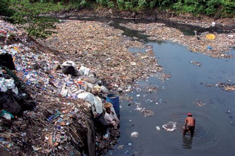 A man washes clothes in a polluted water stream Man