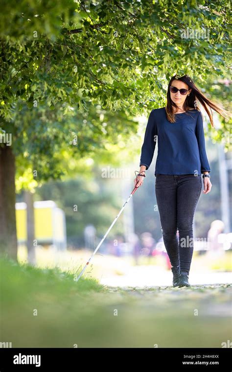 Blind woman walking on city streets, using her white cane to navigate ...