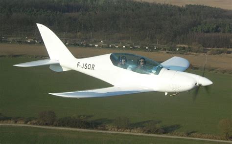 a small white plane flying over a lush green field