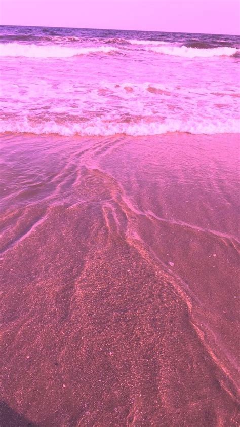 an ocean wave rolls in on the sand at the beach with pink hued water