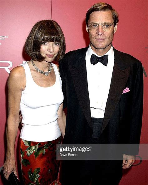 a man and woman standing next to each other in front of a red wall at ...