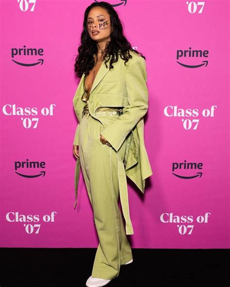 a woman standing in front of a pink wall wearing a green suit and white ...