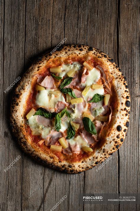 Top view of homemade pizza with slices of ham, pineapple, basil leaves ...