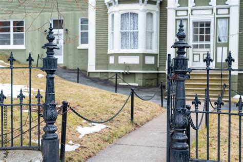 An antique black wrought iron fence with a large tree and row houses in ...