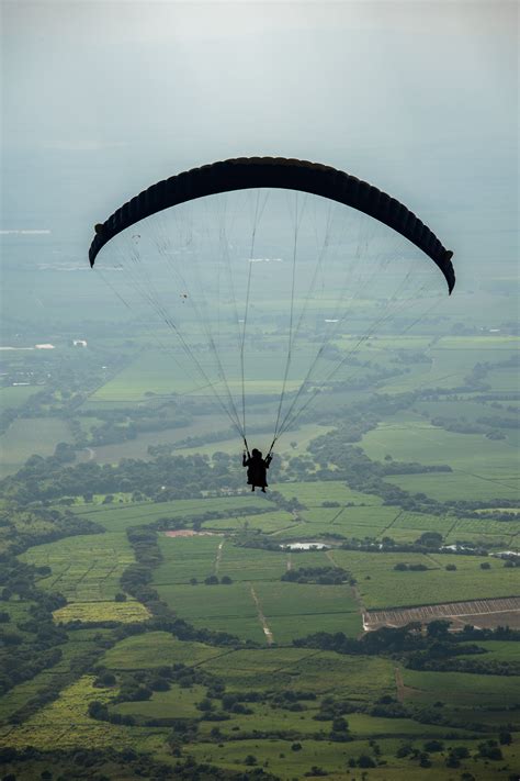 Faceless person flying paraglider over green countryside · Free Stock Photo