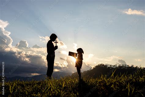 Silhouette of children holding cross and book praying at the sunset ...