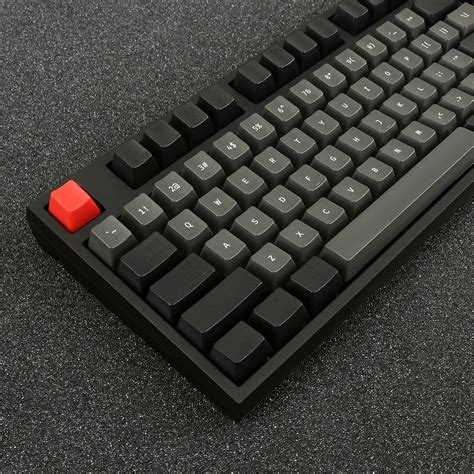 a computer keyboard sitting on top of a black table next to a red mouse pad