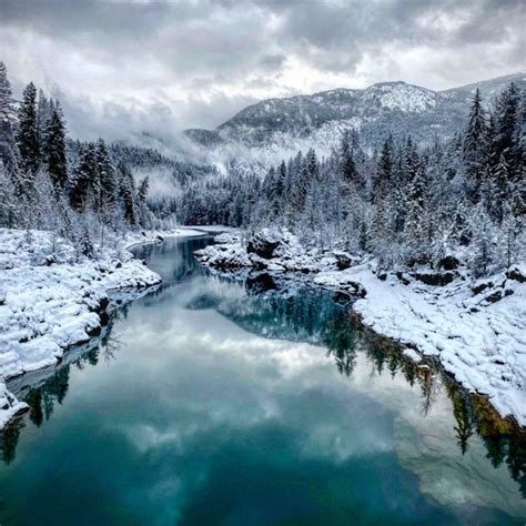 a river surrounded by snow covered mountains and evergreen trees in the ...