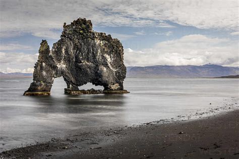 Volcanic rock formation in the shallows on a black sand beach ...