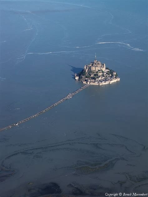 an island in the middle of water with a castle on it's top and walkway