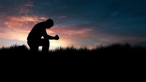 4-26-CH Silhouette of man kneeling in prayer in field at sunset