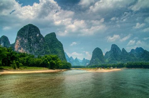 a river with mountains in the background and green trees on both sides ...