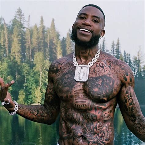 a man with tattoos on his chest standing in front of a lake