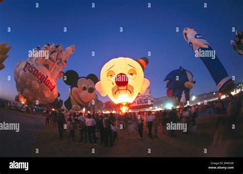 crowd of people watch as hot-air-balloons including clown, Mickey Mouse ...