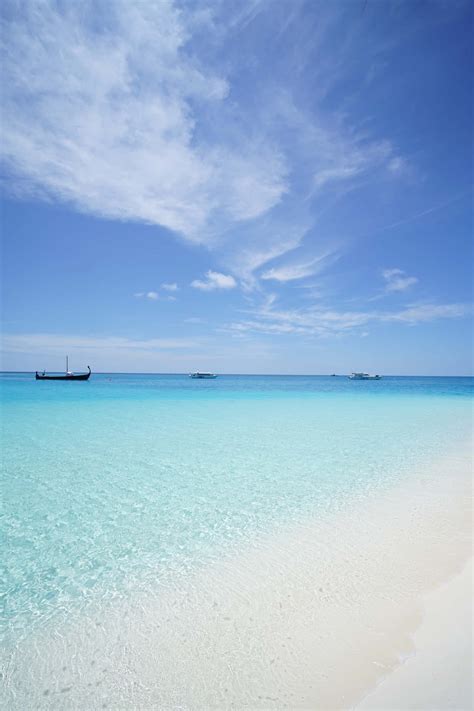 Download A Beach With Clear Water And A Boat In The Distance Wallpaper ...