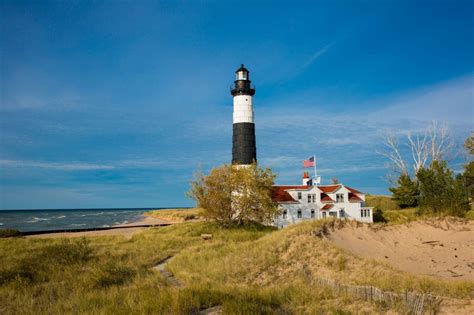 Black and white striped lighthouse in beach dunes on the coast.