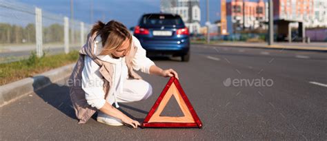 a woman driver puts an emergency stop sign near a broken car, traffic ...