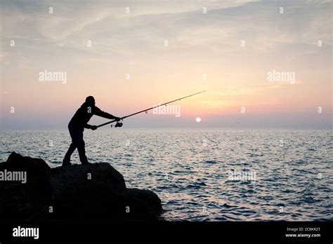 Silhouette of man fishing at sunset Stock Photo - Alamy