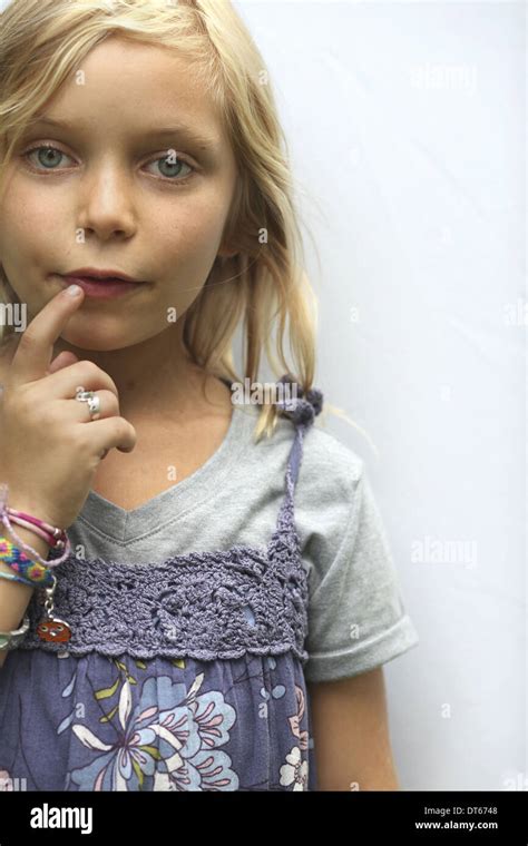 A young girl with blonde hair, and blue eyes. Her hand to her mouth ...