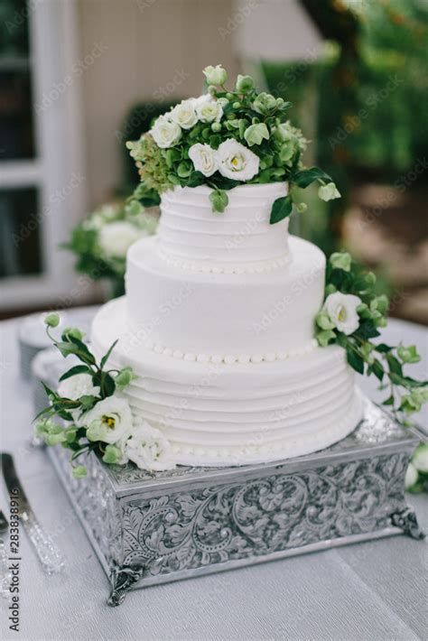 bride and groom cutting white wedding cake with green and white flowers ...