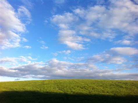 a grassy field under a blue sky with white clouds in the distance and a ...