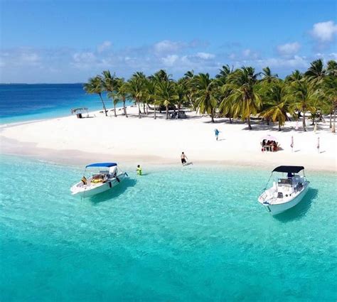 two small boats in the water near a beach with palm trees and people on it