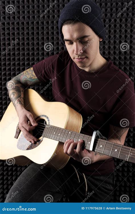 A Guy with Tattoos in a Dark T-shirt and Hat is Playing on the Guitar ...