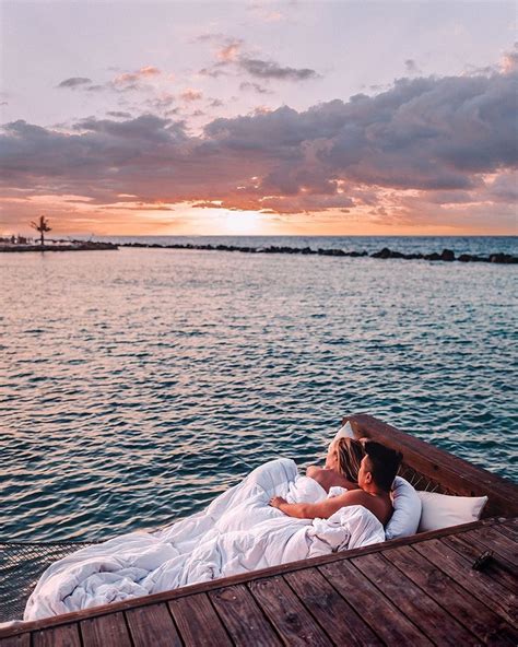 two people are laying on a boat in the water at sunset, with one person ...