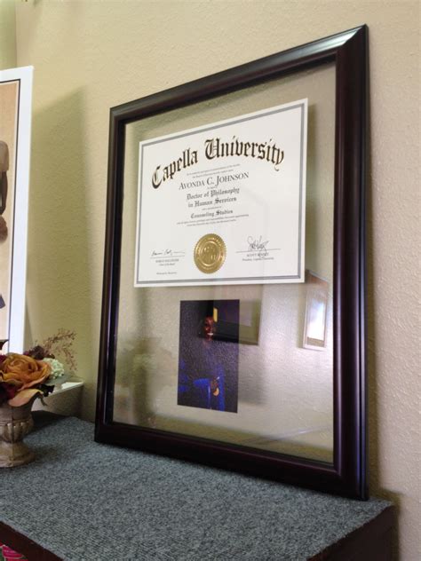 there is a framed diploma and vase with flowers on the shelf in front of it