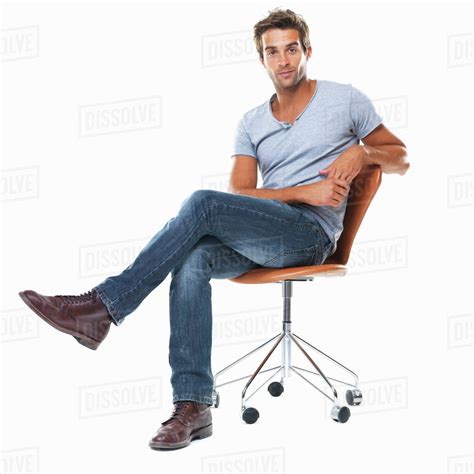 Portrait of young man sitting on chair with legs crossed against white ...