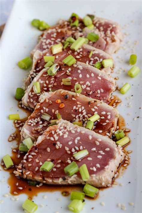 three pieces of meat on a white plate with sesame seeds and green ...