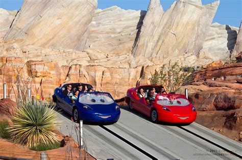 two cars are going down the track in front of some mountain side rocks ...