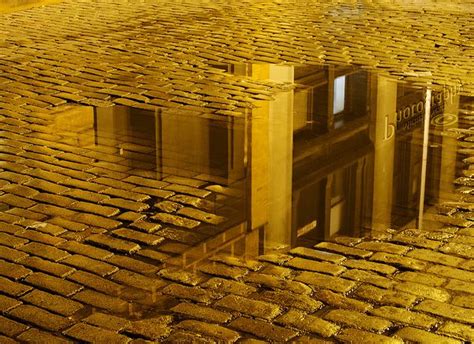 the reflection of a building in water on cobblestone pavement with ...