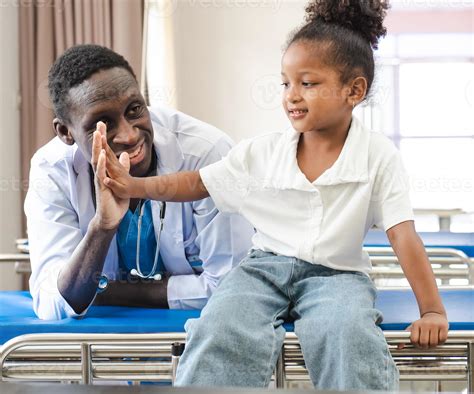 niño paciente sentado en la cama del hospital con un médico africano ...