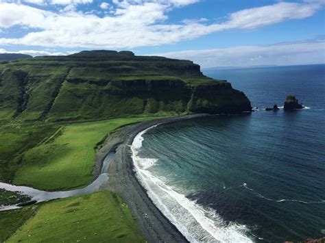 an aerial view of the ocean with cliffs in the distance and green grass ...