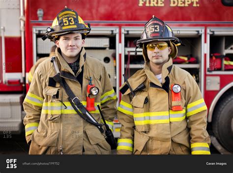 Two firefighters standing in front of a fire engine stock photo - OFFSET