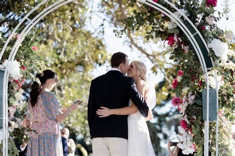 a bride and groom kissing under an arch decorated with flowers