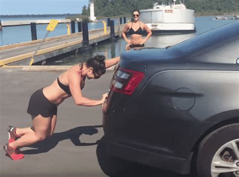 two women in swimsuits are working on the hood of a car near a boat dock