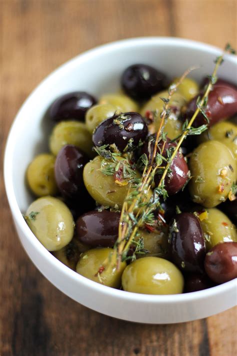 a white bowl filled with green and black olives on top of a wooden table