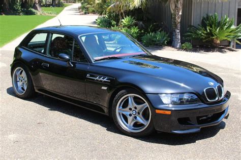 a black bmw car parked in front of a house with palm trees and bushes ...