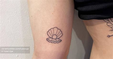 Minimalist oyster and pearl tattoo on the inner arm.