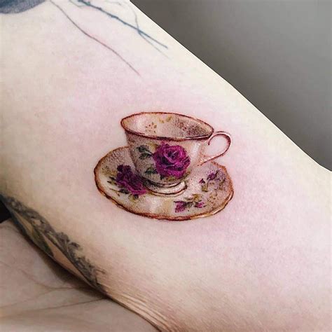 a cup and saucer tattoo on the right side of the left arm, with pink ...