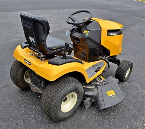 a yellow riding lawn mower sitting on top of a parking lot next to a ...