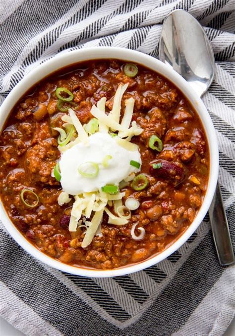 a white bowl filled with chili and sour cream on top of a striped towel ...