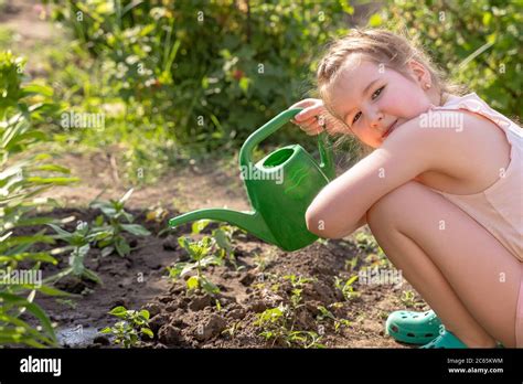 Lovely smiling little girl outdoor in garden takes care of plants by ...