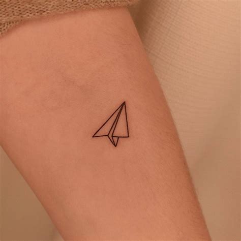 Minimalist paper airplane tattoo on the inner forearm.