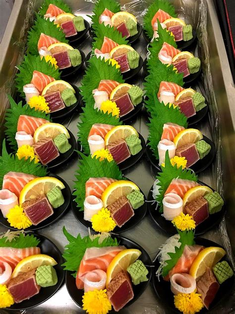 sushi platters are arranged on black plates with green leaves and ...