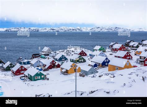 Colorful inuit houses among rocks and snow at the fjord in a suburb of ...